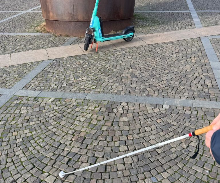 Beim überqueren eines Platzes stehen Kunstwerke und ein Scooter im Weg und erschweren den Weg zum Ziel.